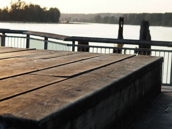 Empty bench on footpath by lake against sky