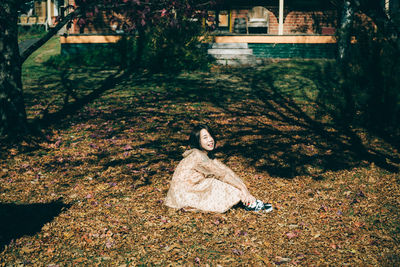 Portrait of smiling mid adult woman sitting on field in park during autumn