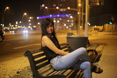 Young woman sitting on bench at night