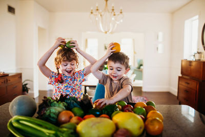 Two happy kids playing with fruits and veggies in kitchen