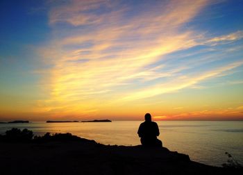 Silhouette man sitting on beach against sky during sunset