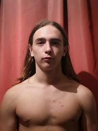 Portrait of shirtless young man standing against red curtain