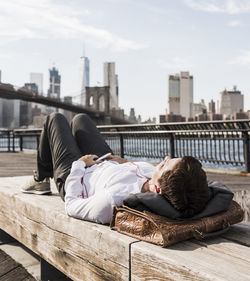 Usa, brooklyn, businesswoman lying on bench listening music with earphones