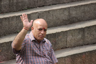 Portrait of man waving hand while sitting on steps