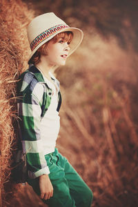 Side view of teenage girl wearing hat leaning on hay at farm