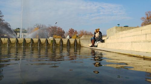 Mother with child looking at fountain while sitting on steps by pond