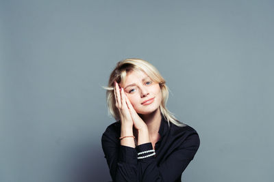 Portrait of young woman with hands clasped against gray background