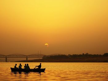 Silhouette people sitting in boat on sea against sky during sunset