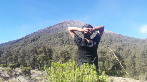 Rear view of man with arms raised on mountain against sky