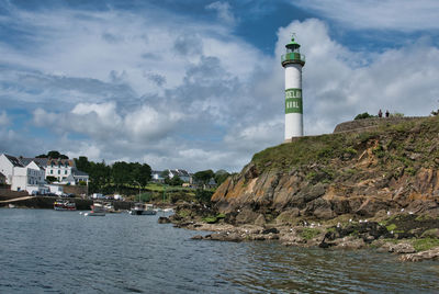 Lighthouse amidst buildings and sea against sky