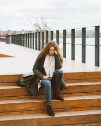 Woman using smart phone while sitting on steps against sky