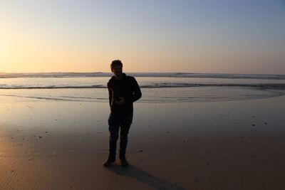 Full length of man standing on beach against sky during sunset