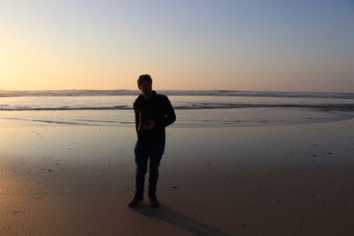 Full length of man standing at beach against sky during sunset