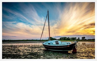 Sailboats moored in sea against sky during sunset