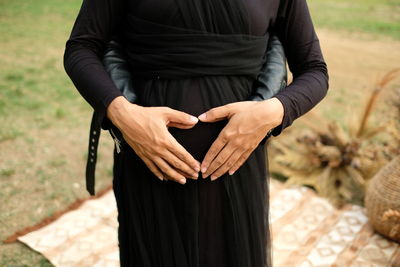 Maternity photo with the theme of black clothes and hands forming love on the stomach