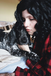 Close-up of tensed young woman holding dog on bed at home