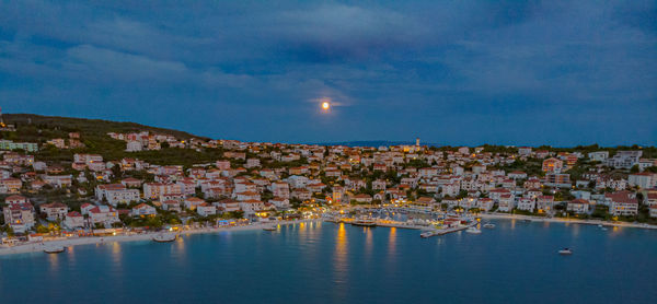 Aerial view of townscape by sea against sky at dusk