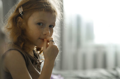 Smiling cute girl sitting on bed in front of window at home