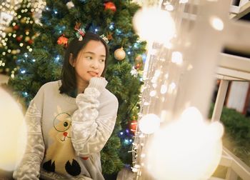 Portrait of young woman standing by christmas tree