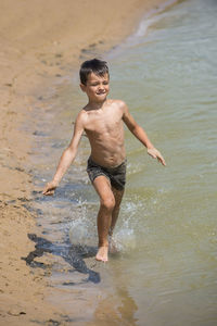 Playful shirtless boy running on shore at beach