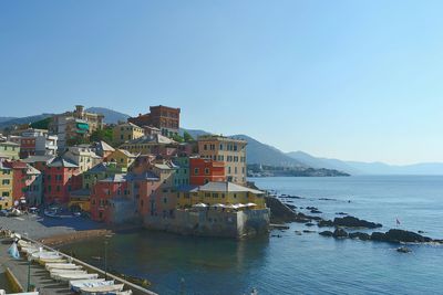 Buildings by sea against clear blue sky