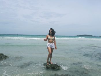 Full length of young woman standing at beach against sky