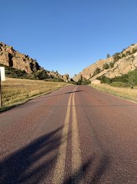 Road leading towards mountains against clear sky