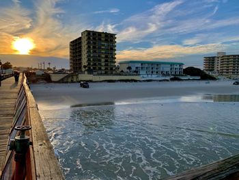 Scenic view of sea by buildings against sky during sunset