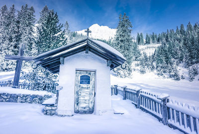 Snow covered house in forest against sky