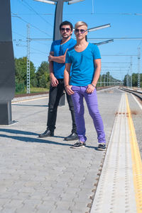 Full length portrait of young couple standing on road against sky