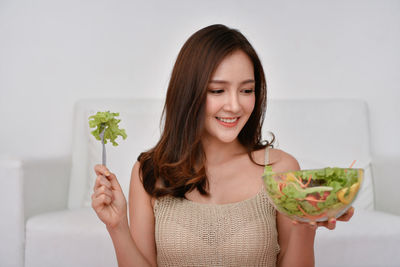 Smiling beautiful woman holding salad bowl at home
