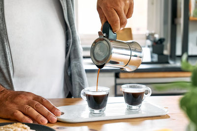 Man preparing classic italian coffee mocha, pouring coffee from moka pot into glass coffee cup.