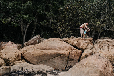 Shirtless father helping daughter in walking on rocks