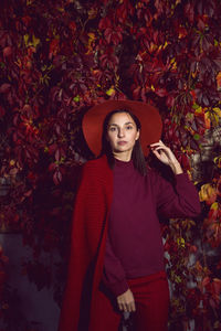 Woman in a red hat and red sweater stands on a background of orange leaves grapes wall autumn