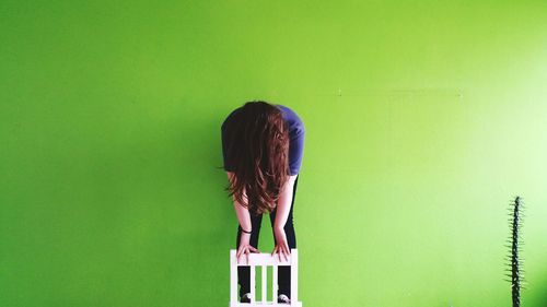 Woman standing on chair against green wall at home