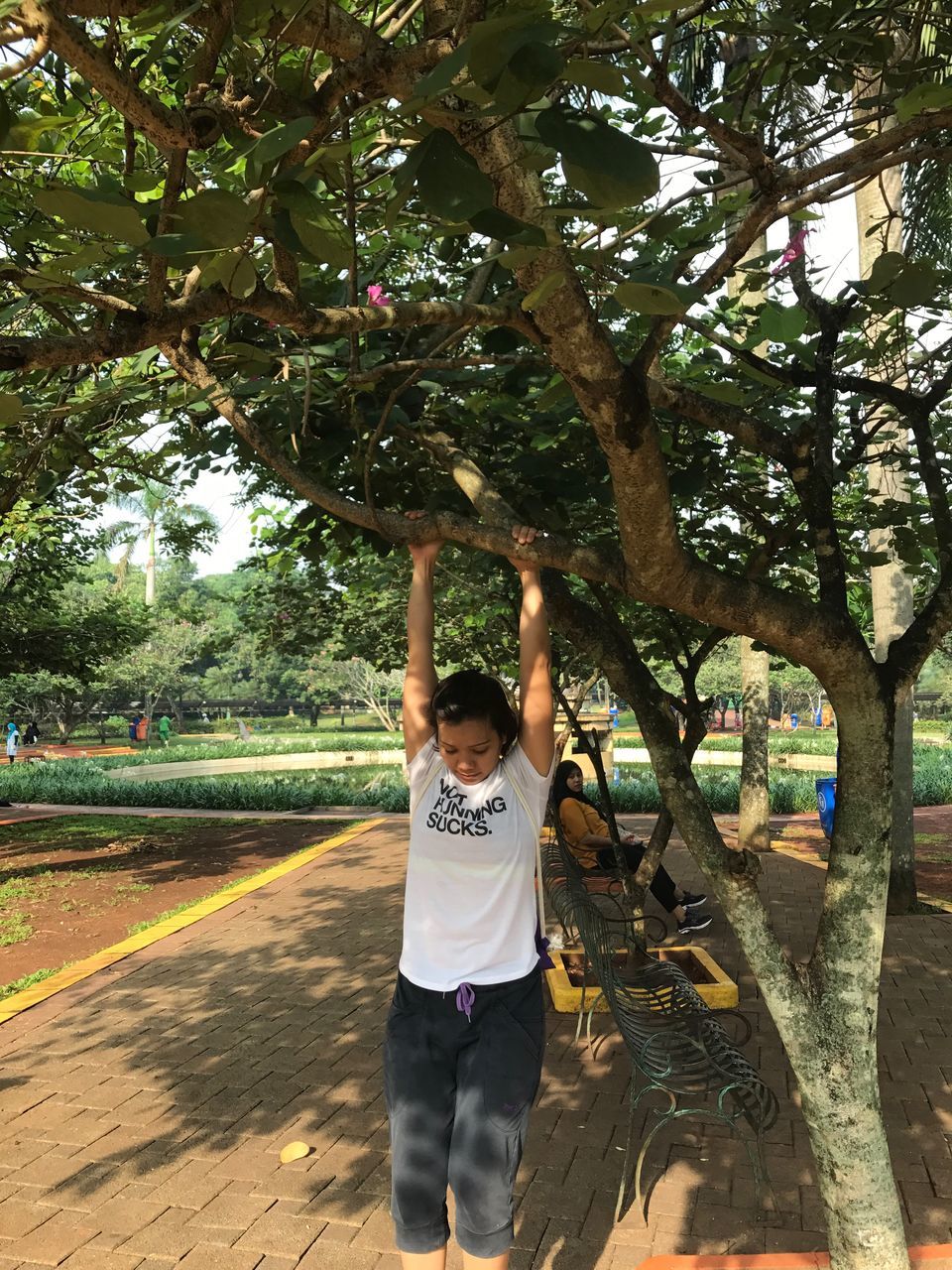 tree, real people, arms raised, lifestyles, leisure activity, casual clothing, one person, front view, park - man made space, growth, day, boys, childhood, full length, elementary age, standing, outdoors, young women, young adult, happiness, playing, branch, nature