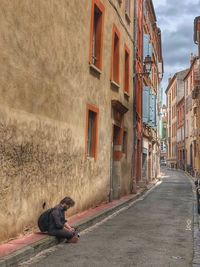 Man sitting in alley amidst buildings in city