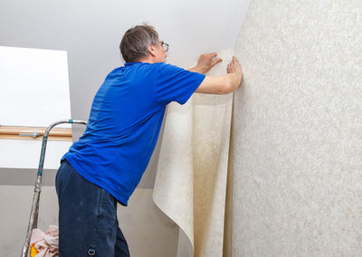 Side view of painter putting wallpaper on wall at construction site