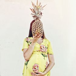 Midsection of woman holding fruit while standing against white background