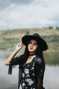 Portrait of young woman standing at lakeshore against sky