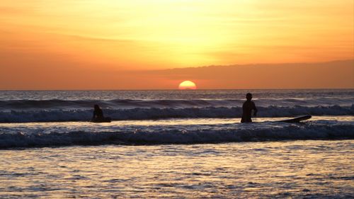 Silhouette surfers on sea against sky during sunset