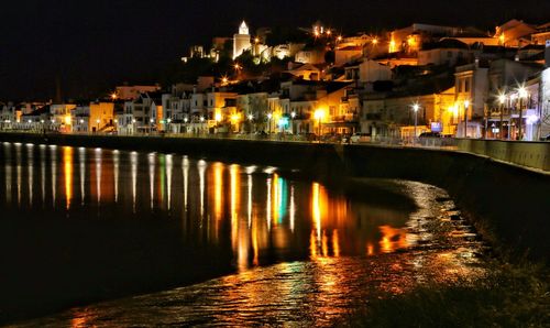 Illuminated buildings by river against sky at night