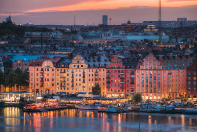 Illuminated buildings by river against sky at sunset