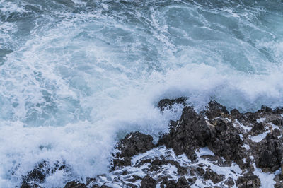 High angle view of waves splashing on rocks at beach