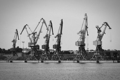 Cranes in shipping dock at sea against sky