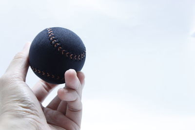 Cropped hand holding baseball against clear sky