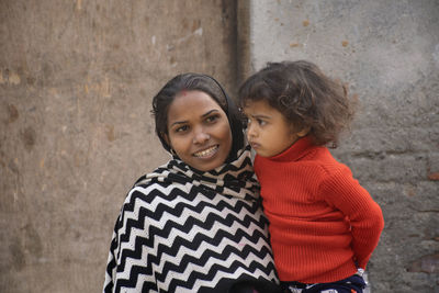 Smiling mother carrying daughter against wall