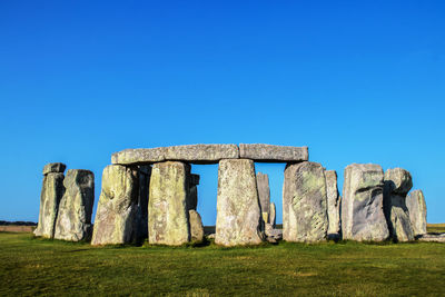 Stone structure on field against clear blue sky
