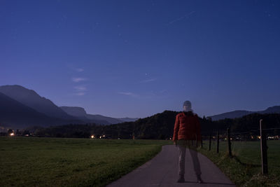 Digital composite image of man standing on road against mountains at dusk