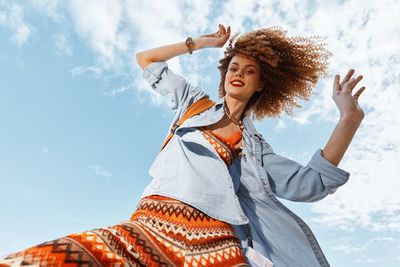 Young woman with arms raised standing against sky